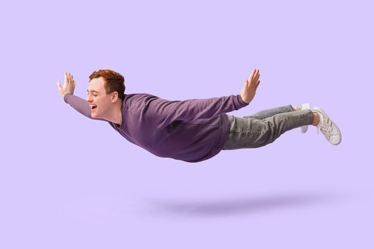 Joyful young man flying on lilac background