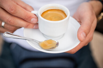 Close-up of hands holding a cup of espresso with a spoon