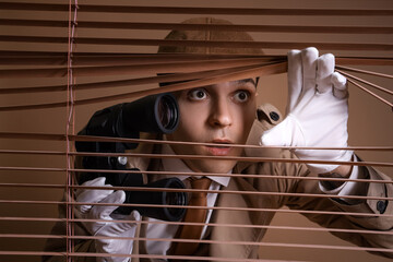 Male spy with binoculars looking through blinds on brown background, closeup