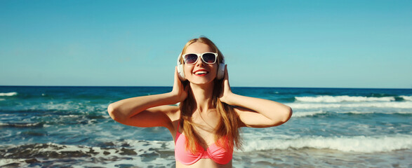 Summer vacation of relaxed happy young woman listening to music with headphones on the beach at sea