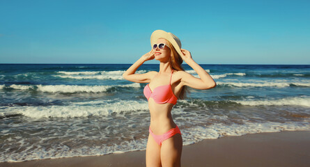 Summer vacation, beautiful happy slim woman in pink bikini swimsuit, tourist hat on the beach on sea