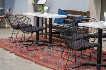 A view of an outdoor cafe with black wire chairs and tables on a red and blue patterned rug