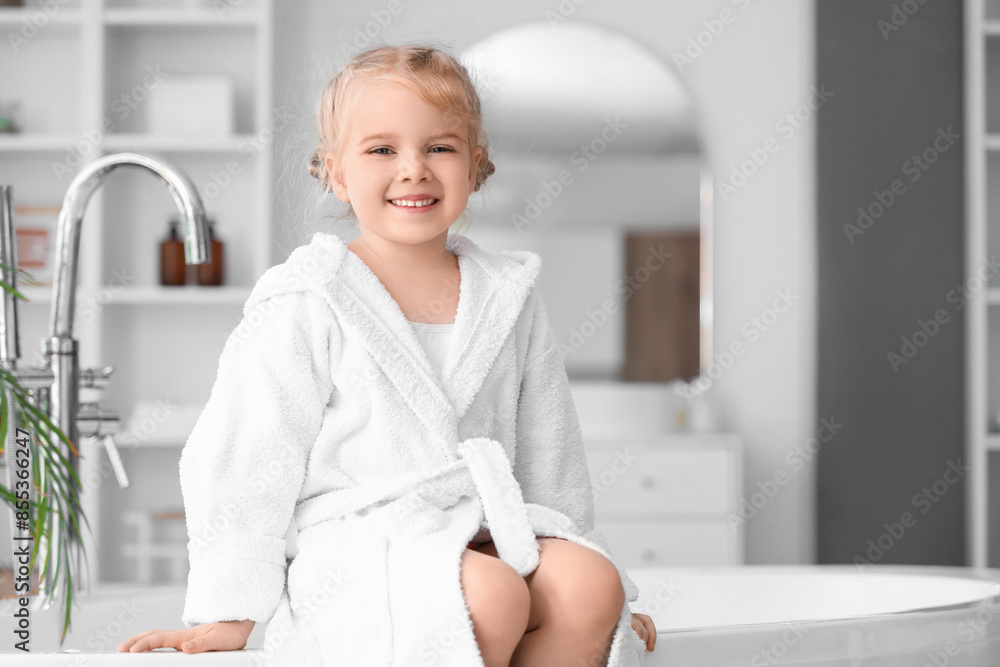 Wall mural Cute little girl in bathrobe sitting on bathtub at home