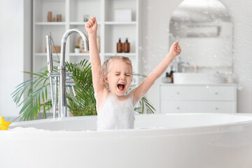 Cute little girl playing with soap bubbles while taking bath in bathroom