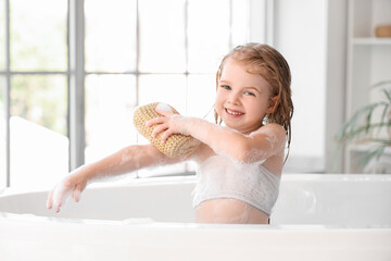 Cute little girl with sponge taking bath in bathroom