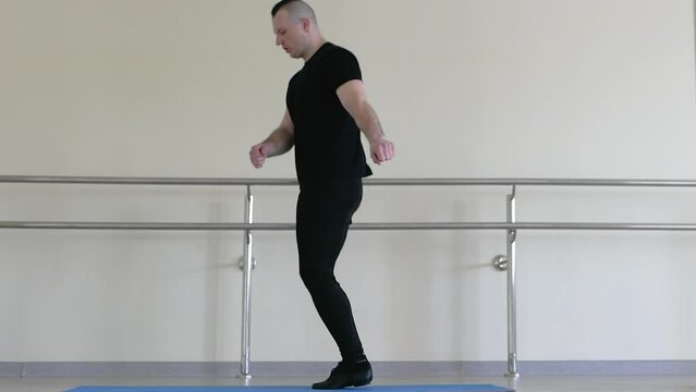 A dancer performs jumps during warm-up during training. Male dancer warming up. Athlete in the fitness room on a gymnastic mat