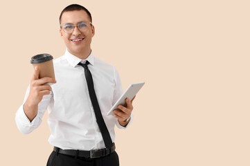 Handsome businessman with tablet computer and coffee cup on beige background