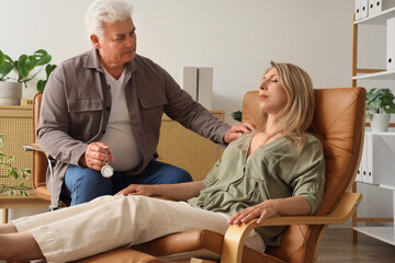 Male psychologist with pocket watch hypnotizing woman on armchair in office