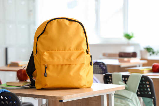 Yellow backpack with apple and copybooks on desk in classroom