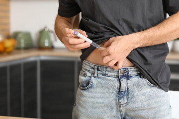 Diabetic young man using lancet pen in kitchen, closeup