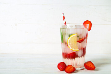 Glass of fresh infused water with strawberries and lemon on white wooden background