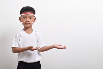 Cute little Asian boy wearing flag headband pointing at the copy space beside him. to celebrate Indonesian Independence Day on August 17 isolated on white background.