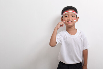 Cute little Asian boy wearing flag headband posing with index finger on cheek solated on white background. Concept of Indonesia's independence day on August 17