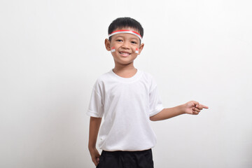 Cute little Asian boy wearing flag headband pointing at the copy space beside himi solated on white background. Concept of Indonesia's independence day on August 17