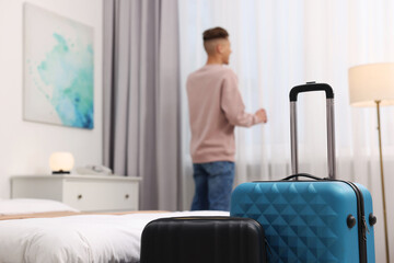 Guest opening curtains in stylish hotel room, focus on suitcases