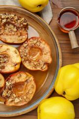 Tasty baked quinces with walnuts and honey in bowl on wooden table, flat lay