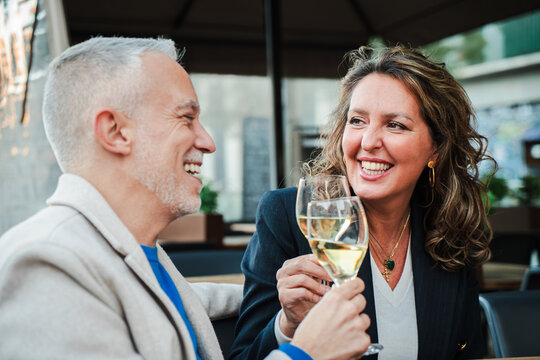Mature couple toasting white wine glasses on a bar terrace. Middle aged married people drinking alcohol on a restaurant. Mid adult friends clinking with alcohol beverages on a date at outdoors pub
