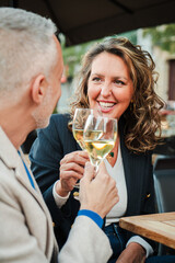 Vertical. Mature couple toasting white wine glasses on a bar terrace. Middle aged married people...