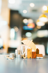 Model of umbrella with house and coins on wooden table concept of the system of insurance savings and the cost of health insurance