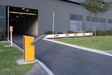 At the entrance of an indoor parking garage, a closed automatic barrier arm or a boom gate operator...