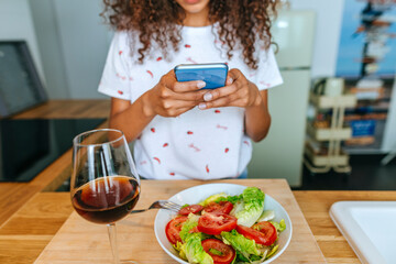 Close-up of woman's hands using mobile phone while eating salting and wine.