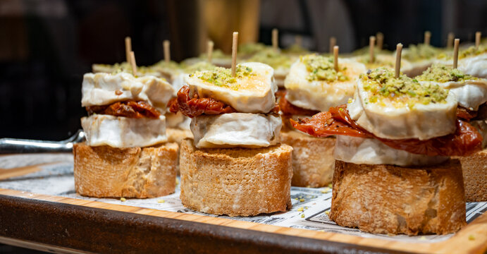 Typical snack of Basque Country, pinchos or pinxtos skewers with small pieces of bread, sundried tomatoes, goat cheese served in bar in San-Sebastian or Bilbao, Spain, close up