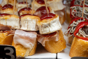 Typical snack of Basque Country, pinchos or pinxtos skewers with small pieces of bread, jamon, goat cheese served in bar in San-Sebastian or Bilbao, Spain, close up