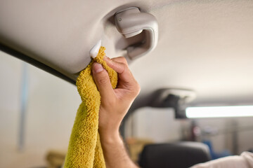 A man is cleaning the cars ceiling meticulously with a yellow cloth, focusing on detail