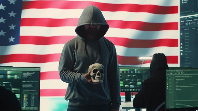 American man in a dark hood making death threats with human skull concept, emphasizing violence and malicious intent. Governmental hacker inflicting terror and panic for rival ideologies. Camera A.