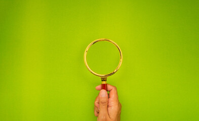 Close-up of hand holding a magnifying glass against a green background.