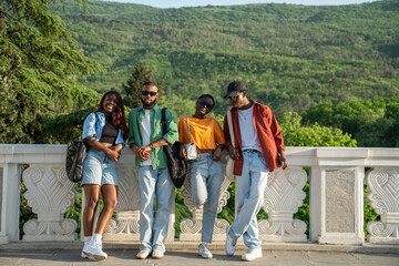 Group of happy African American friends smiling, looking at camera, leaning against concrete fence. Cheerful stylish black students walking together in park, relaxing, chilling, enjoying outside rest 