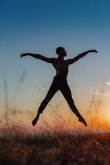 Silhouette of male ballet dancer jumping and doing a majestic dance move in nature, Behind him are heavenly clouds and the sun is setting.