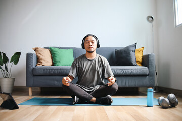 Asian man meditating at home using headphones