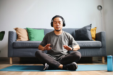 Young man with stubble sitting on yoga mat with eyes closed and relaxing in easy seat pose at home.