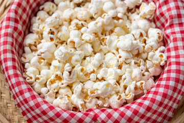 Tilted close-up view of a straw hat with red and white checkered fabric and salted popcorn inside. Typical food for the São João June festival.
