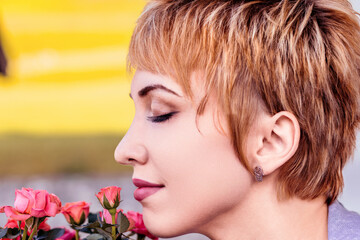 Fototapeta premium Woman with short blond hair smelling roses with eyes closed