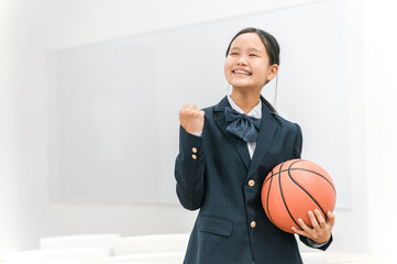 バスケットボールを持ってガッツポーズする制服姿の中学生・高校生の女の子（バスケ部・部活・青春）
