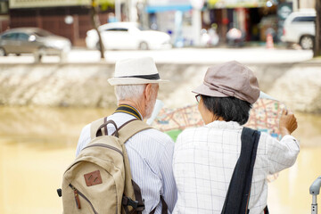 Closeup back view of American senior tourist man with his tour guide are looking at city maps to find tourist attractions on blurred of city background. Senior tourist concept