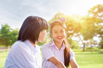 Closeup cheerful Thai students sat talking happily on outdoors school lawn with sun bright and blurred nature background.