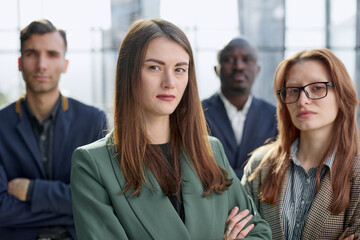 Obraz premium Young executive smiling and standing in a bright room with her team behind her
