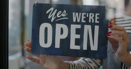 Close-up of female hand waitress hanging Open sign on transparent cafe door inviting customers. Successful business start and catering concept.