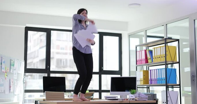 Woman dances barefoot on desk throwing papers around