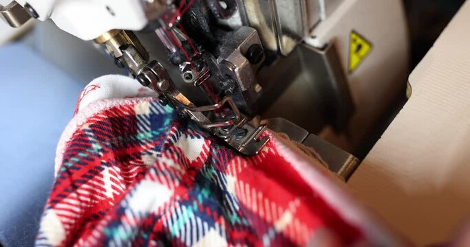 Seamstress straightens fabric under overlock foot at workplace