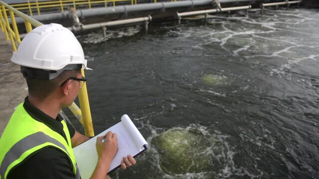an engineer stand aside at the waste water pool and check the list on a clipboard to make sure that the gauge at standard value, waste water treatment