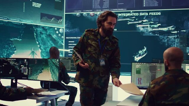 Staff sergeant providing mission files to brief his operational crew, working on gathering intelligence from surveillance systems. Prepares for various combat scenarios and outcomes. Camera B.