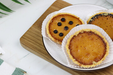Pie Susu Bali or popular egg tart from Bali, Indonesia, served with various topping original and chocolate. Tea time concept with marble background.