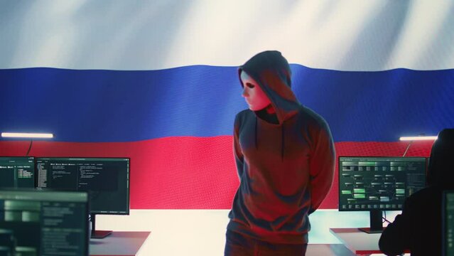 Russian hacker in a governmental IT environment with a russian flag on big screen, dealing with cyber terror, ransomware and espionage. Installing misinformation and aggression propaganda. Camera B.