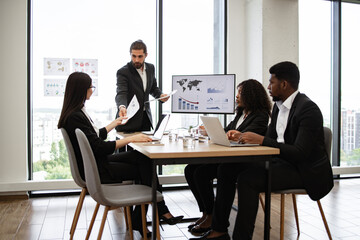 Businessman hands out paper tasks or results of company activities to colleagues during business...