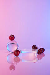 Fototapeta premium The blank showcase pedestal of glass placed in the middle of table, decorated beside with flat lay cherries and a crystal ball, against colorful background. Space for presentation and adding text