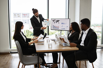Team of professionals in business meeting discussing financial reports and data. Employees engaged in presentation with charts and graphs. High-rise office environment conveys corporate and teamwork.